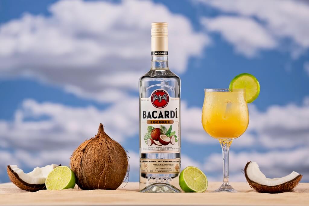 Bacardi Coconut bottle with a cocktail, coconuts, and limes